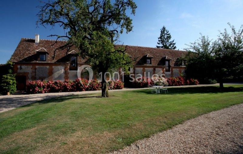 Bâtisse ancienne en pierre avec toit en tuiles, entourée d'arbres, pelouse et allée gravillonnée.