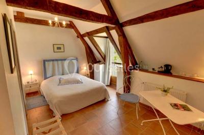 Chambre lumineuse avec poutres apparentes, lit double, table blanche, et vue sur un balcon avec verdure.