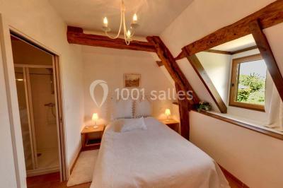 Chambre lumineuse avec poutres apparentes, lit double, table blanche, et vue sur un balcon avec verdure.
