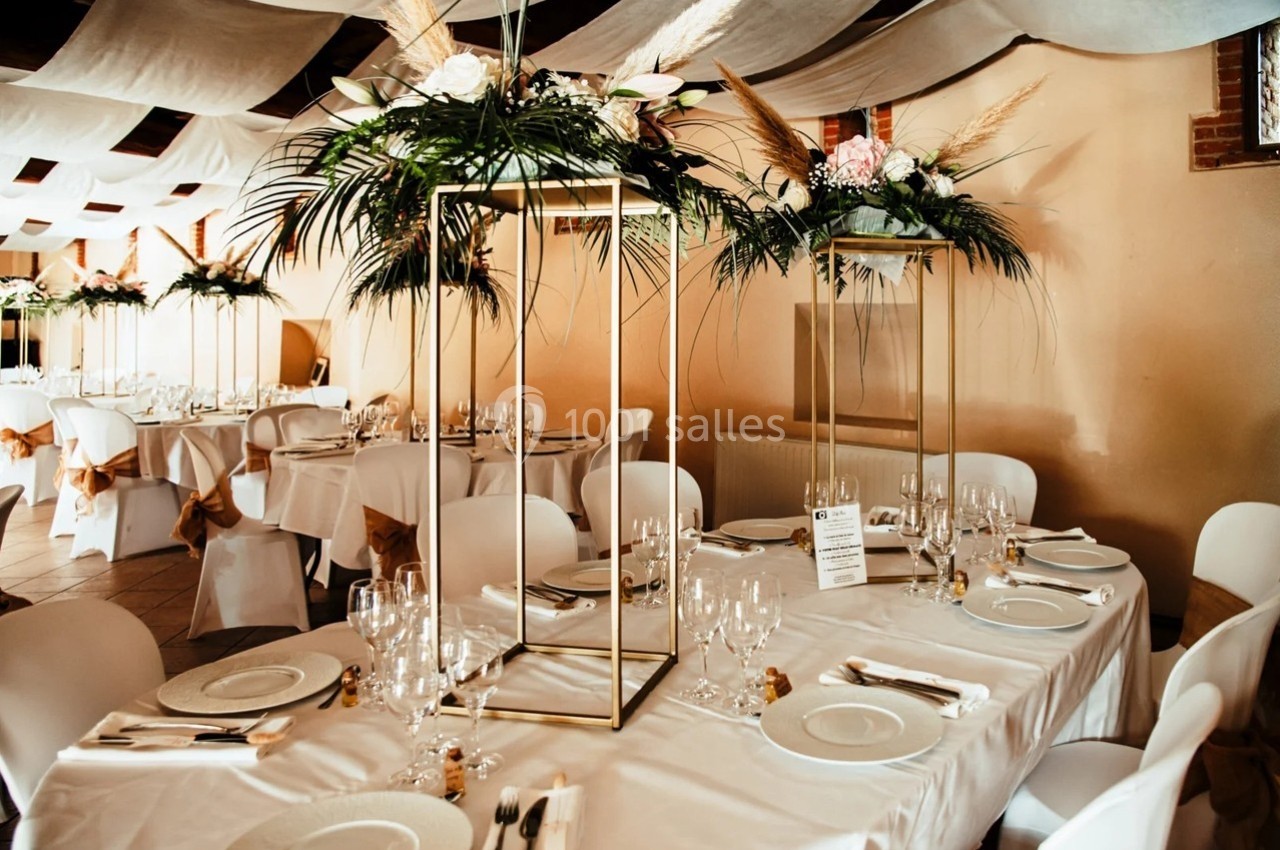 Salle de réception décorée avec des tables dressées, des centres de table floraux et des nappes blanches.
