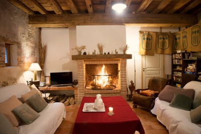 Chambre mansardée lumineuse avec lit simple, poutres apparentes, fenêtre, table de chevet et étagère en bois.