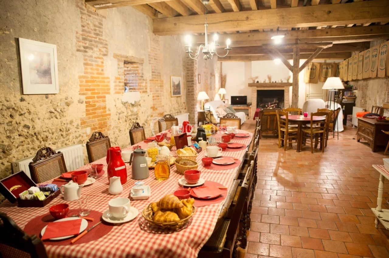 Grande table dressée avec nappes à carreaux rouges, petit-déjeuner servi dans une salle rustique avec murs en pierre.