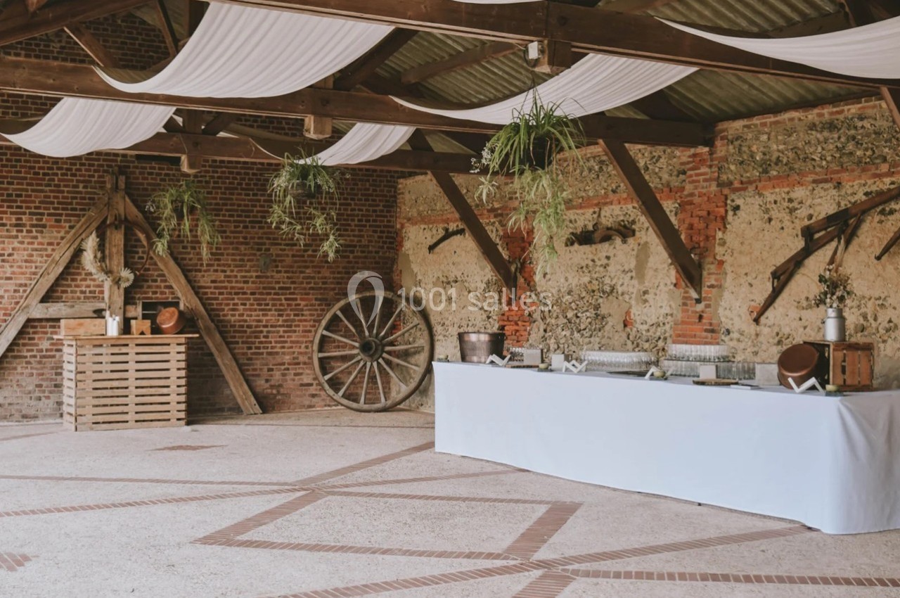 Salle rustique avec murs en briques, charpente en bois, décorations suspendues et tables pour un événement.