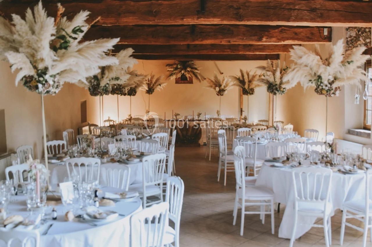 Salle de réception décorée avec des tables rondes, nappes blanches et arrangements de pampas.