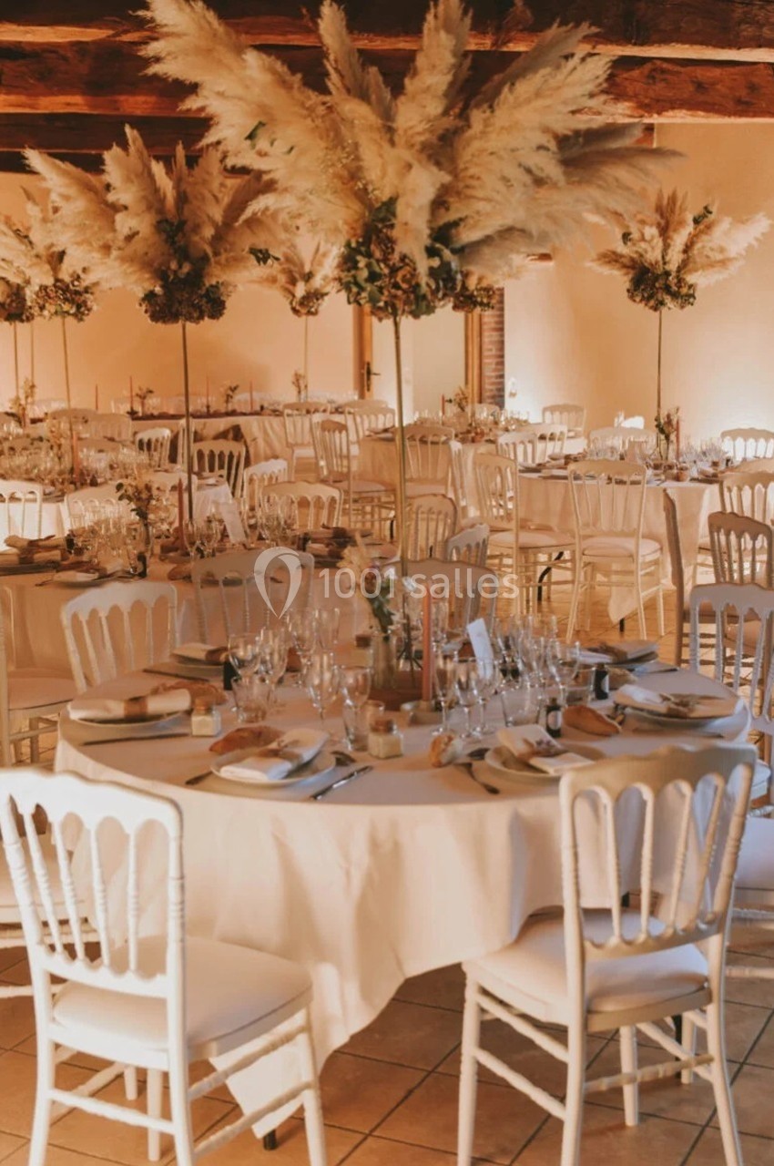 Salle de réception décorée avec des tables rondes, nappes blanches, chaises assorties et centres de table en pampas.