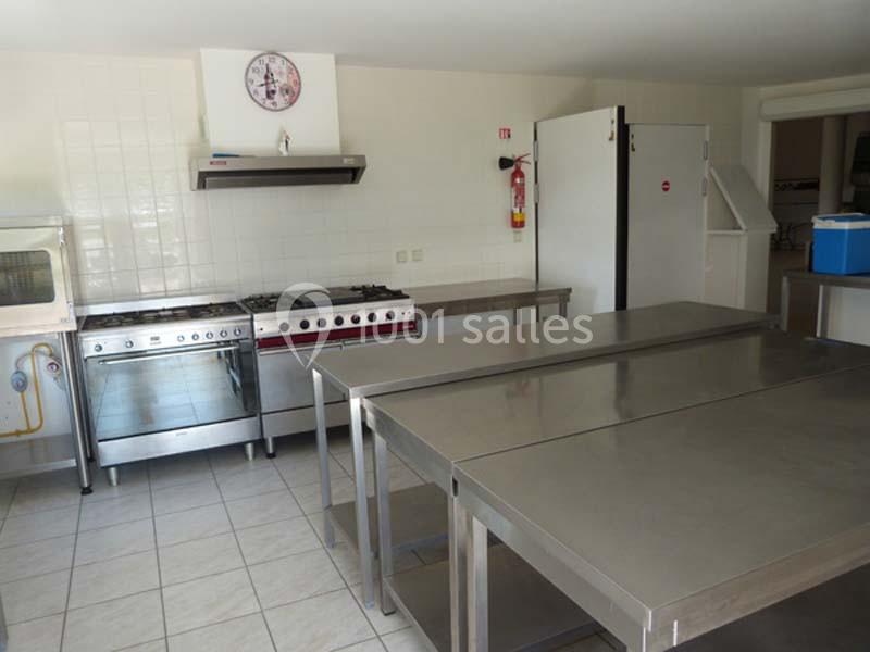 Cuisine professionnelle équipée avec plans de travail en inox, cuisinières, four, réfrigérateur et horloge murale.