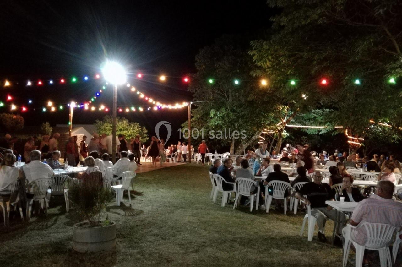 Personnes assises et debout lors d'une fête nocturne en extérieur, éclairée par des guirlandes lumineuses colorées.
