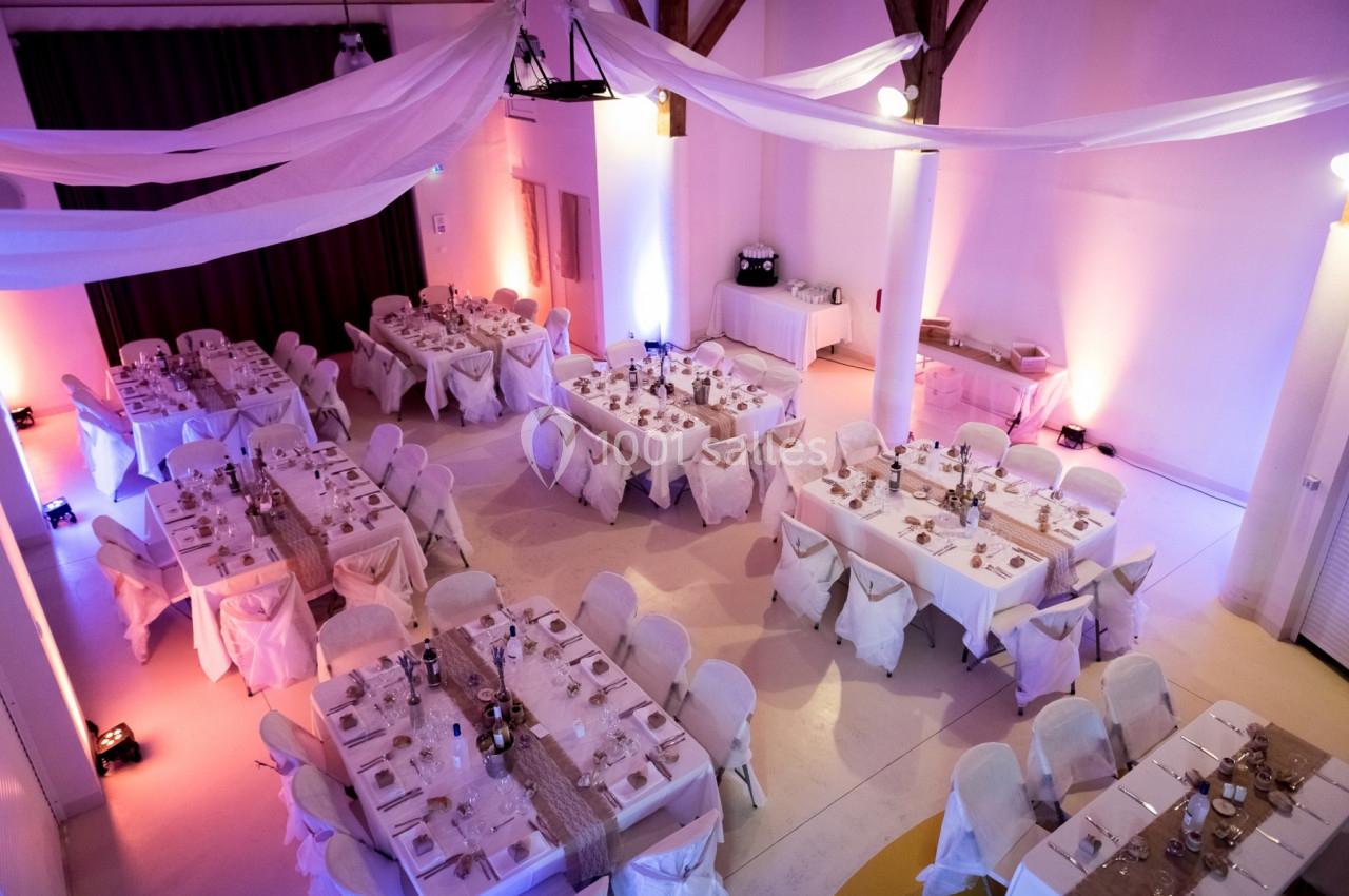 Salle de réception décorée avec des tables dressées, nappes blanches et éclairage chaleureux.
