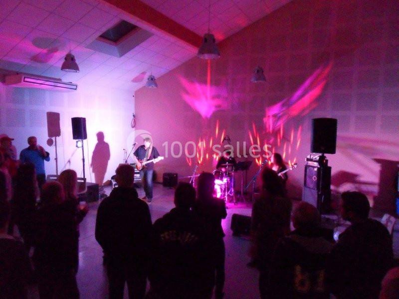 Groupe de musiciens jouant sur scène dans une salle éclairée par des lumières colorées, avec un public debout.