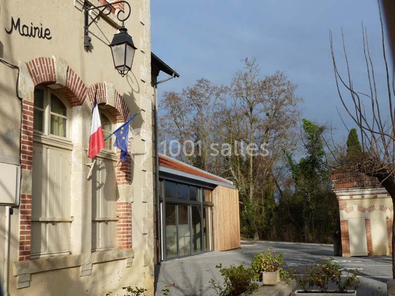 Façade d'une mairie en pierre avec drapeaux français et européen, entourée d'arbres et d'un bâtiment moderne adjacent.