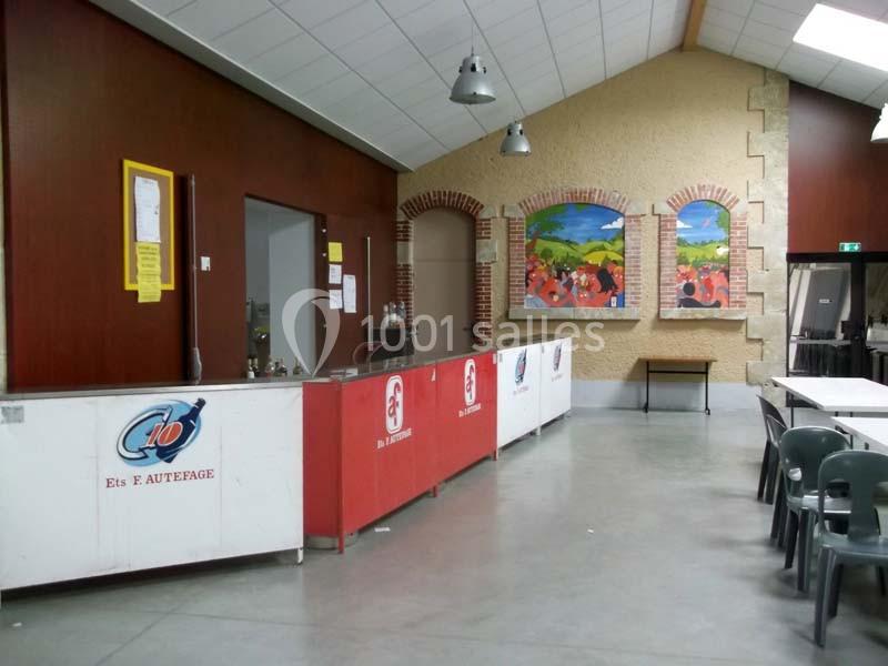 Intérieur d'une salle avec un comptoir, des chaises empilées et des fresques colorées sur un mur en pierre.