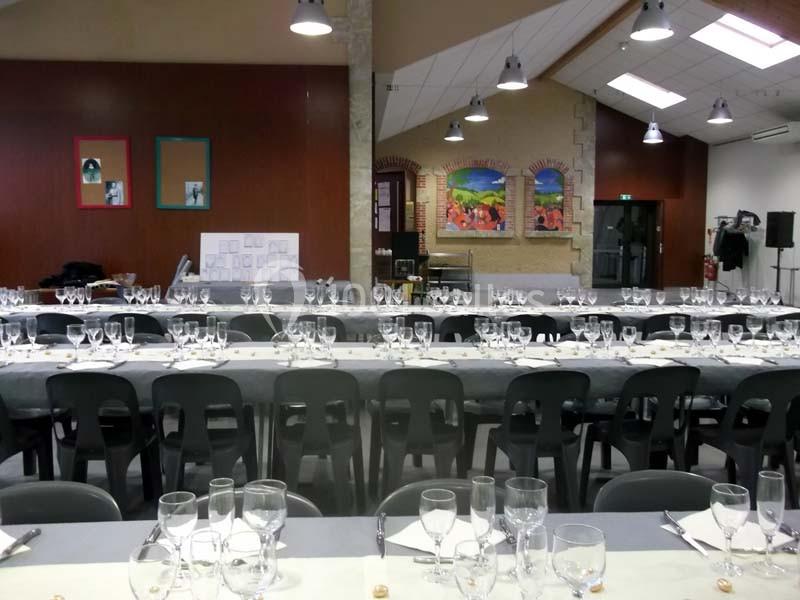 Tables dressées avec nappes grises, verres et couverts dans une grande salle lumineuse au décor mural coloré.