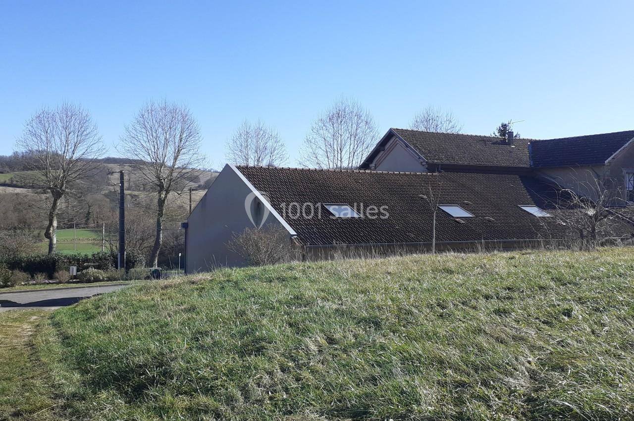 Maison avec toit en tuiles entourée de champs et d'arbres, sous un ciel bleu dégagé.
