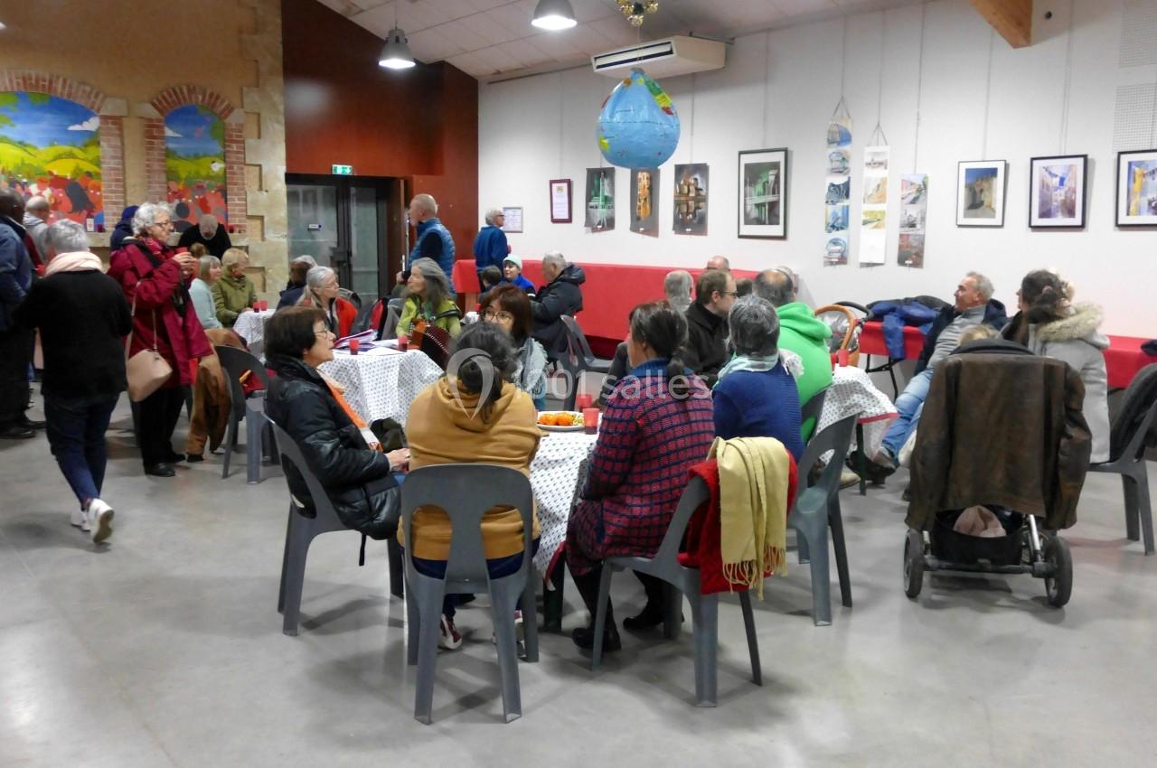 Des personnes assises et debout discutent dans une salle conviviale avec des tables, des chaises et des décorations murales.