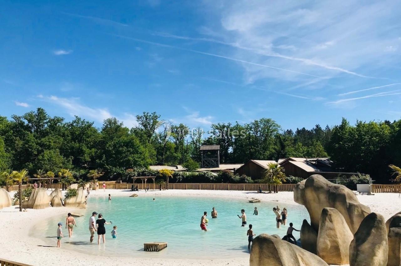 Personnes se baignant dans un lagon artificiel entouré de sable blanc, de rochers et de végétation verdoyante.