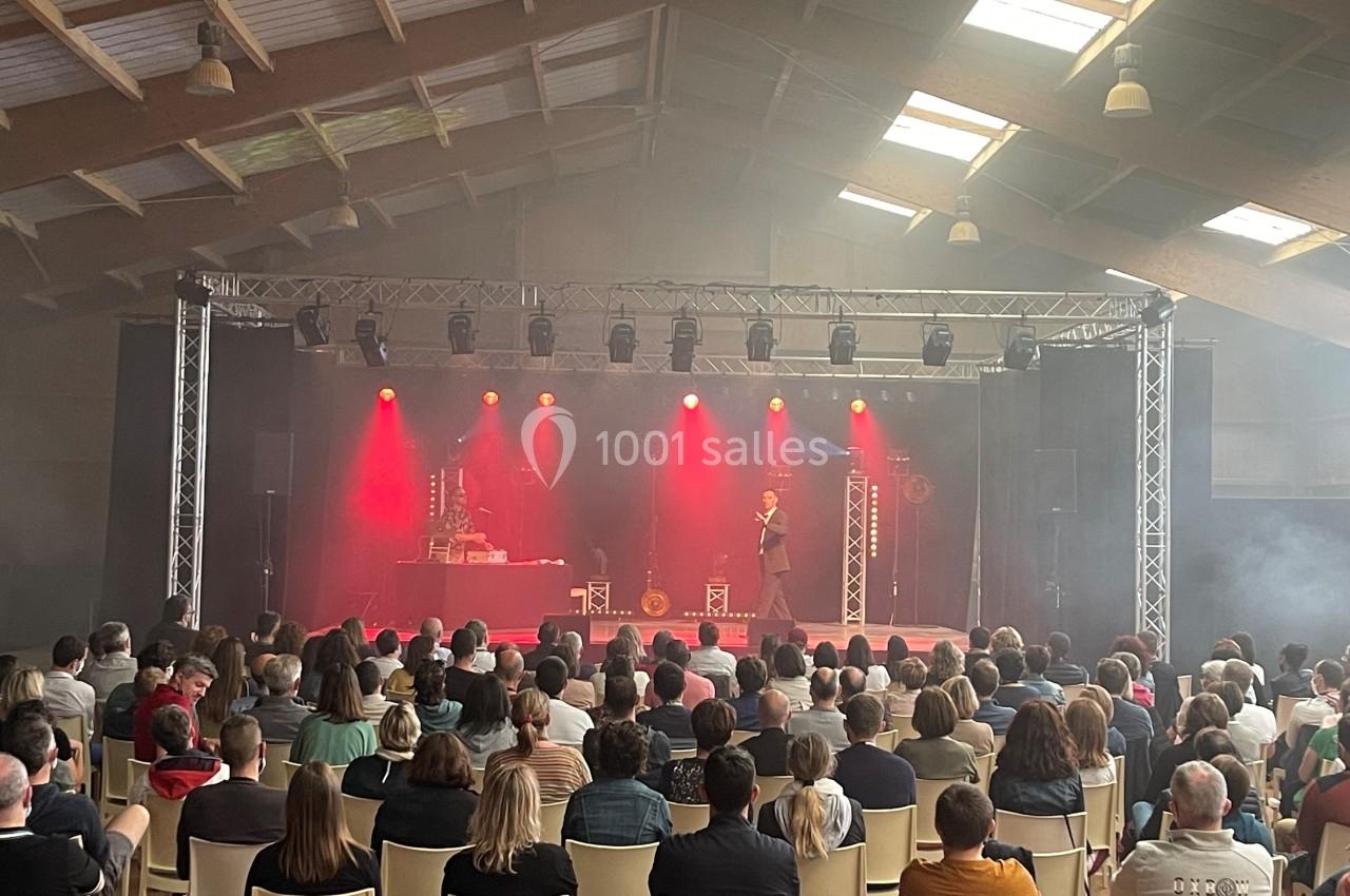 Un magicien réalise un spectacle sur une scène éclairée en rouge, face à un public assis dans une salle.