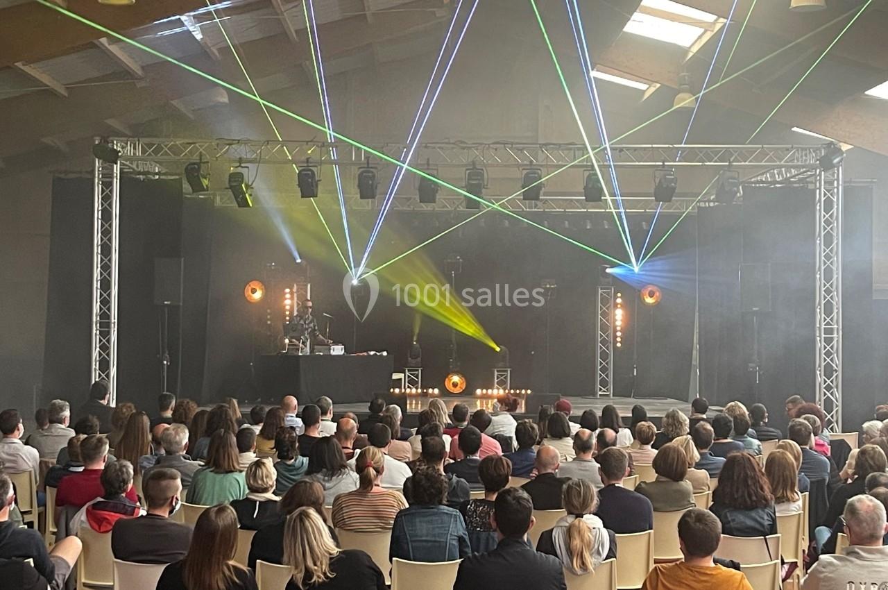 Un public assis regarde un spectacle avec jeux de lumière et lasers dans une salle sombre.
