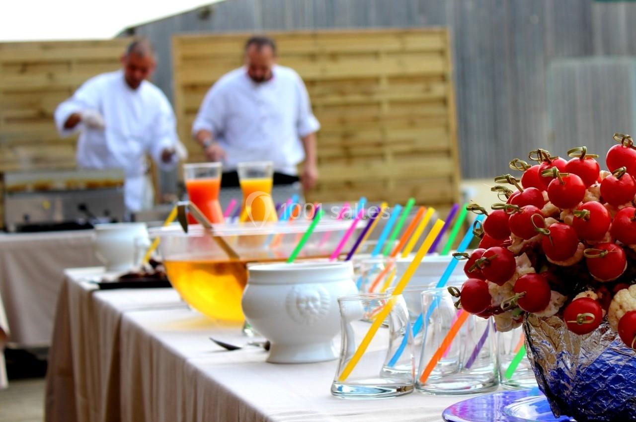 Buffet en extérieur avec boissons colorées, brochettes de tomates cerises et deux chefs en arrière-plan.