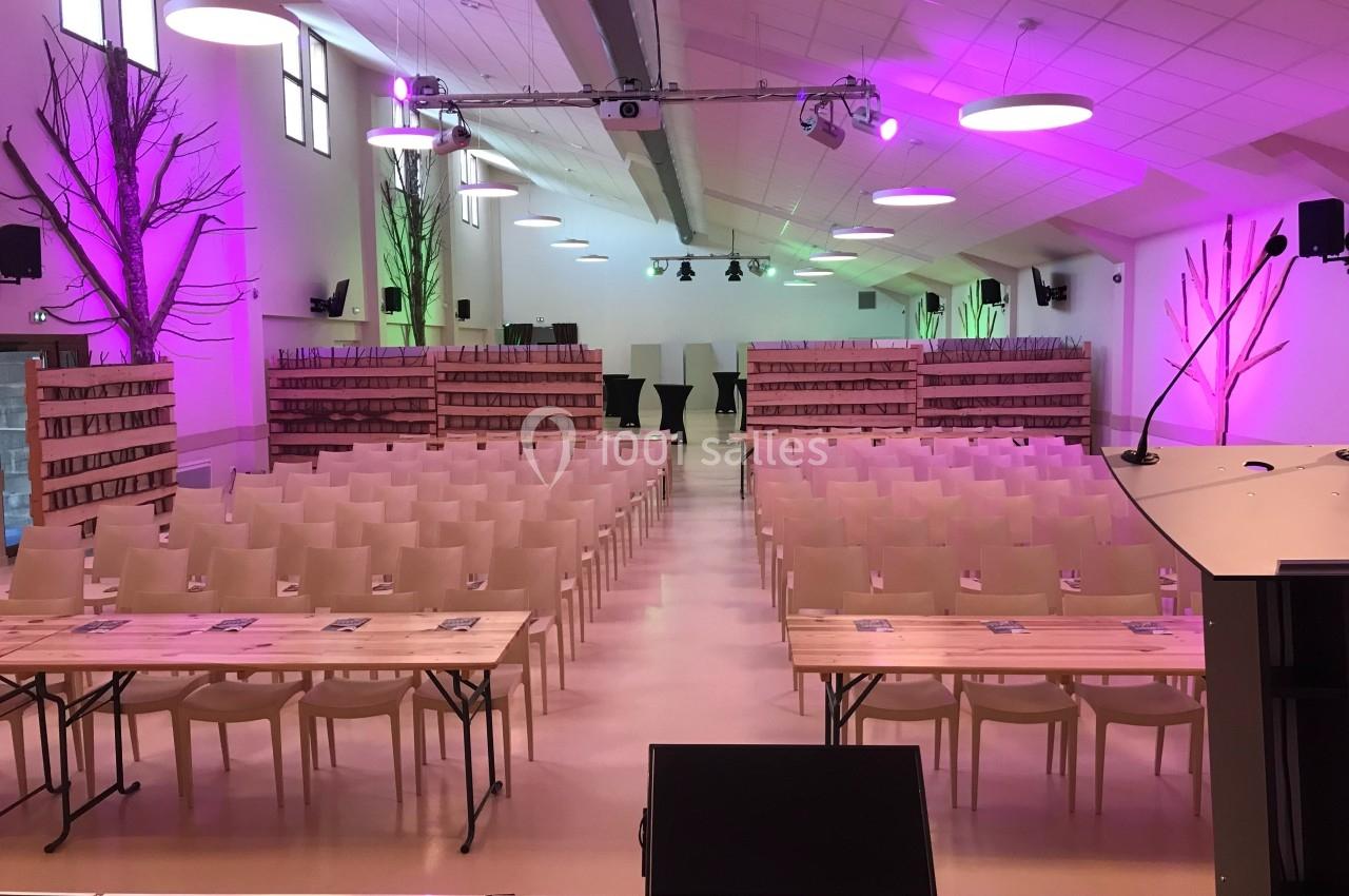 Salle de conférence aménagée avec des rangées de chaises, des tables et un éclairage coloré rose et vert.
