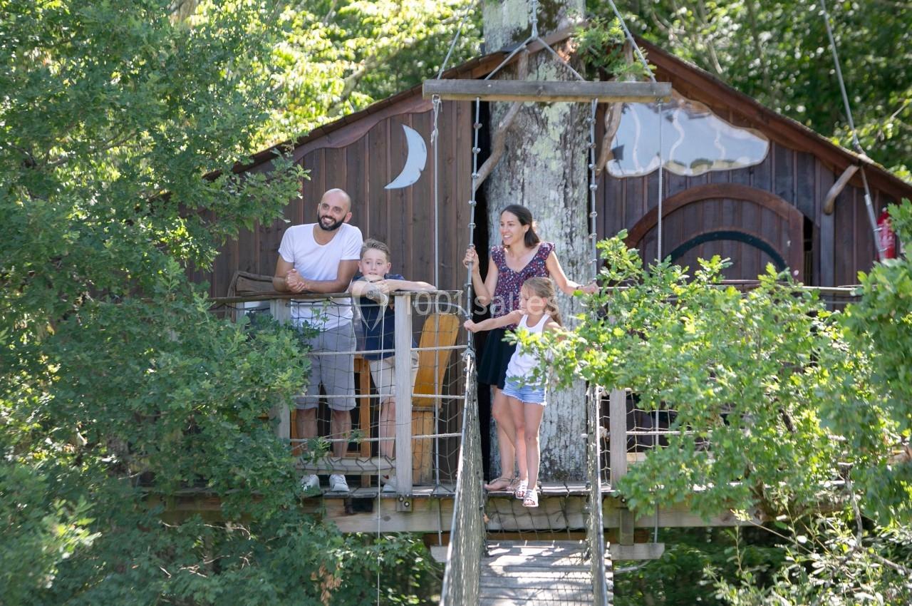 Une famille debout sur la terrasse d'une cabane perchée dans un arbre, entourée de feuillage.