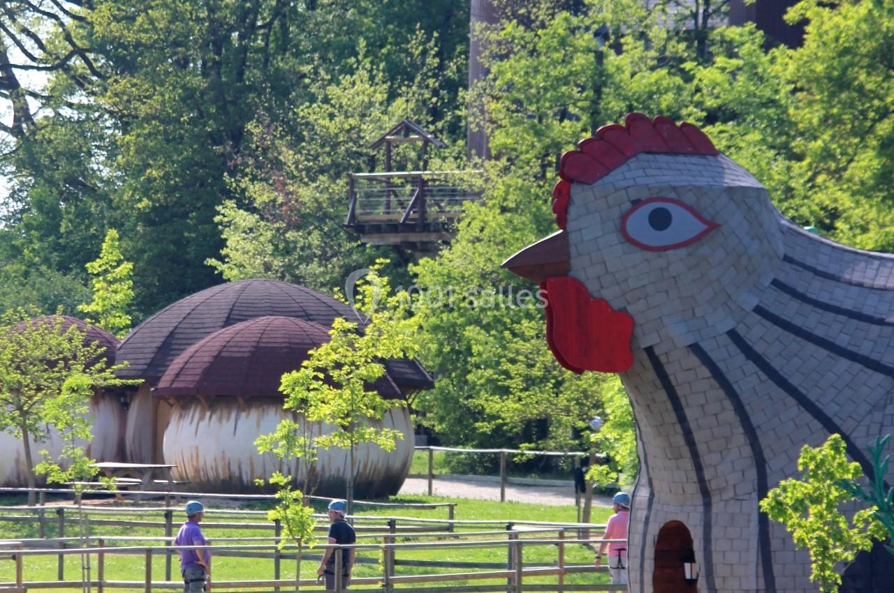 Parc avec des structures en forme de poule et de champignons, entouré de verdure et de visiteurs se promenant.