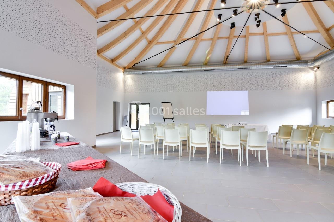 Salle lumineuse avec chaises disposées face à un écran de projection, table en premier plan avec paniers et serviettes…