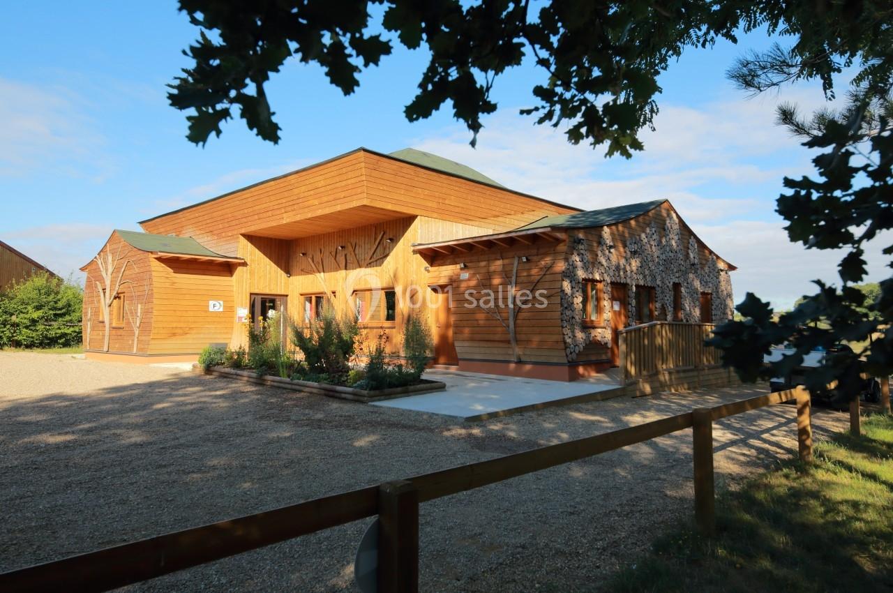 Bâtiment en bois moderne entouré de végétation, avec une allée gravillonnée et un ciel dégagé en arrière-plan.