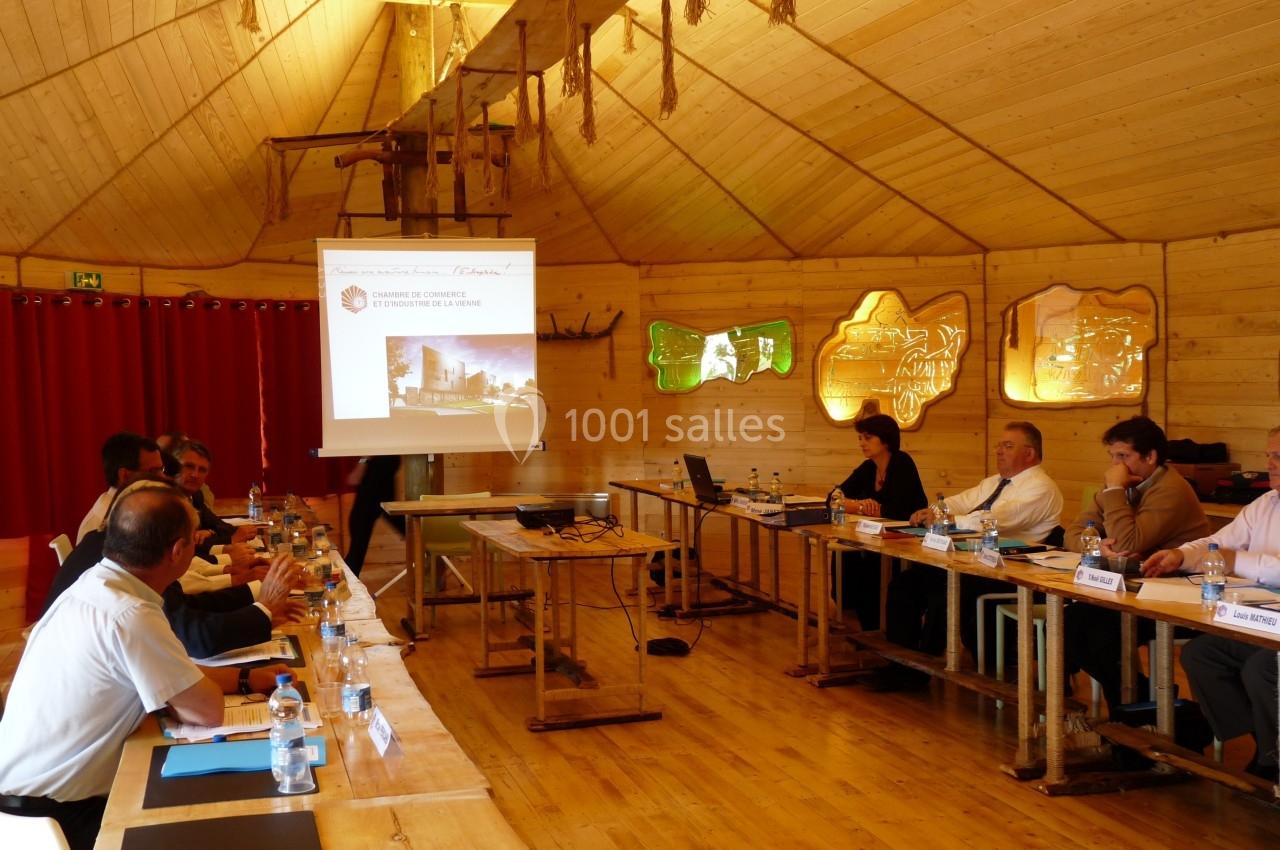 Réunion dans une salle en bois avec des participants assis autour de tables et une présentation projetée sur écran.