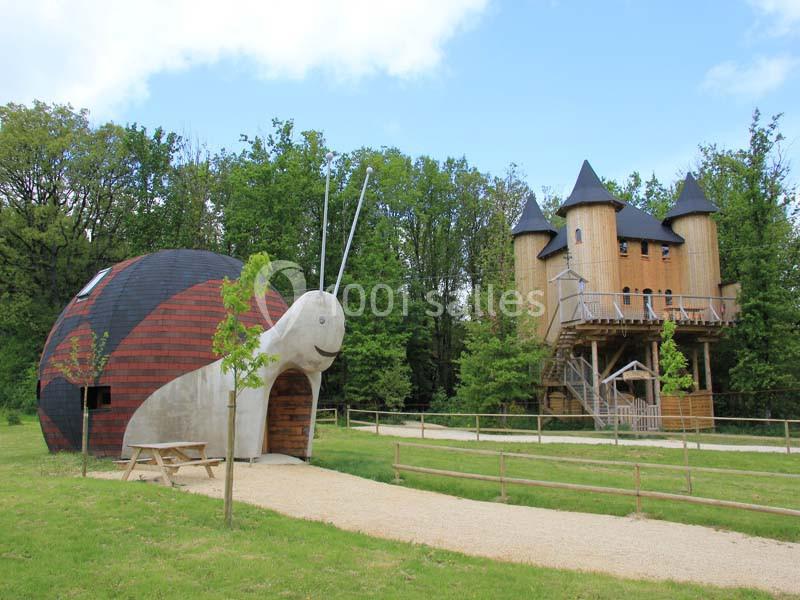 Une maison en forme d'escargot et un château en bois entourés d'arbres dans un cadre naturel.