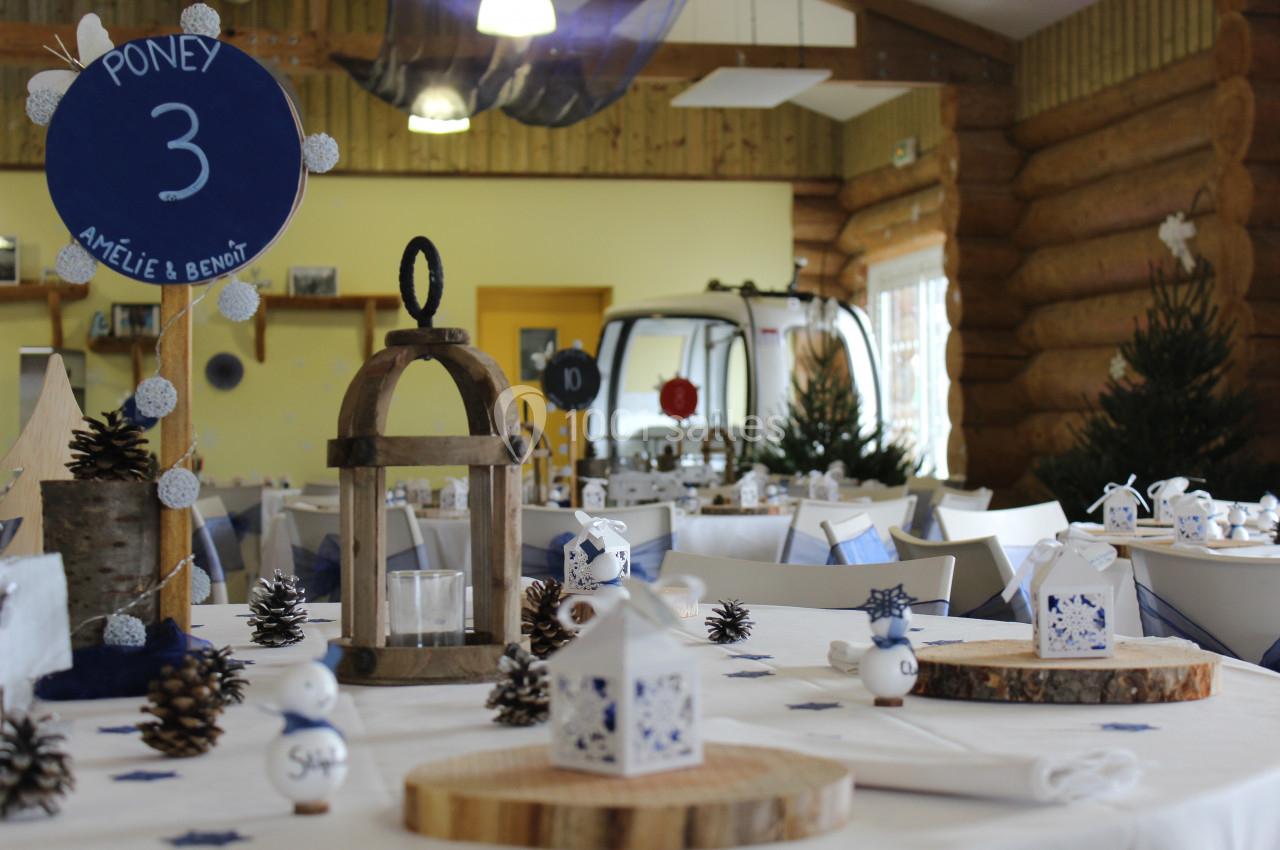 Salle décorée pour un événement avec des tables dressées, des lanternes en bois, des rondins et des éléments hivernaux.
