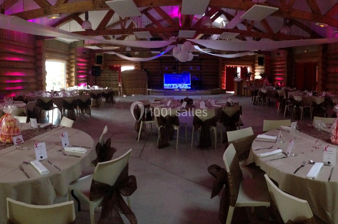 Salle de réception décorée avec des tables rondes dressées, éclairage tamisé et ambiance chaleureuse.