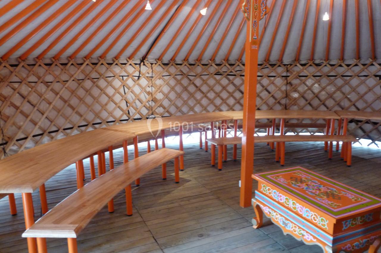 Intérieur d'une yourte avec des bancs en bois disposés en arc de cercle et une table décorée au centre.