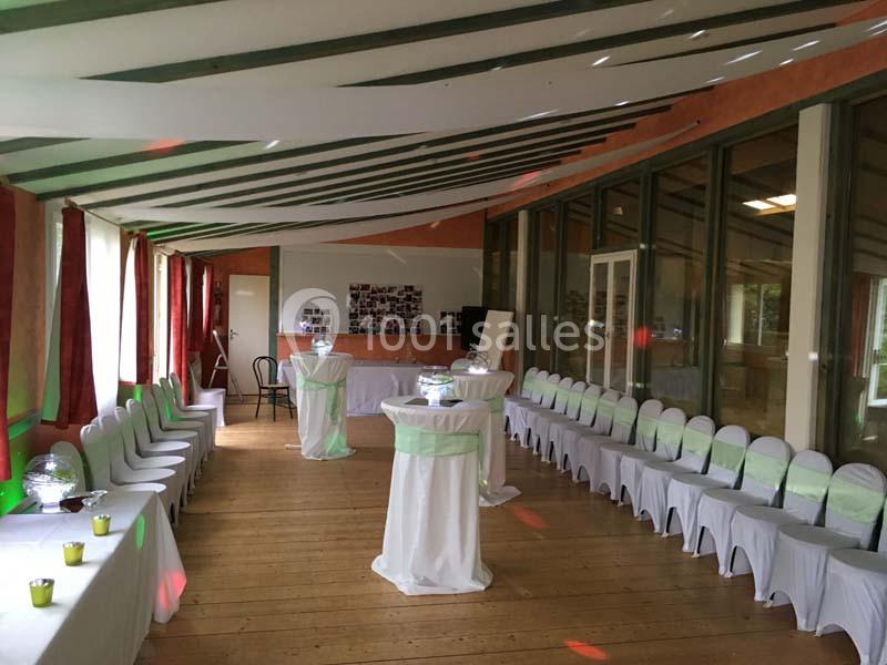 Salle décorée pour un événement, avec chaises blanches alignées, tables hautes et murs ornés de photos.