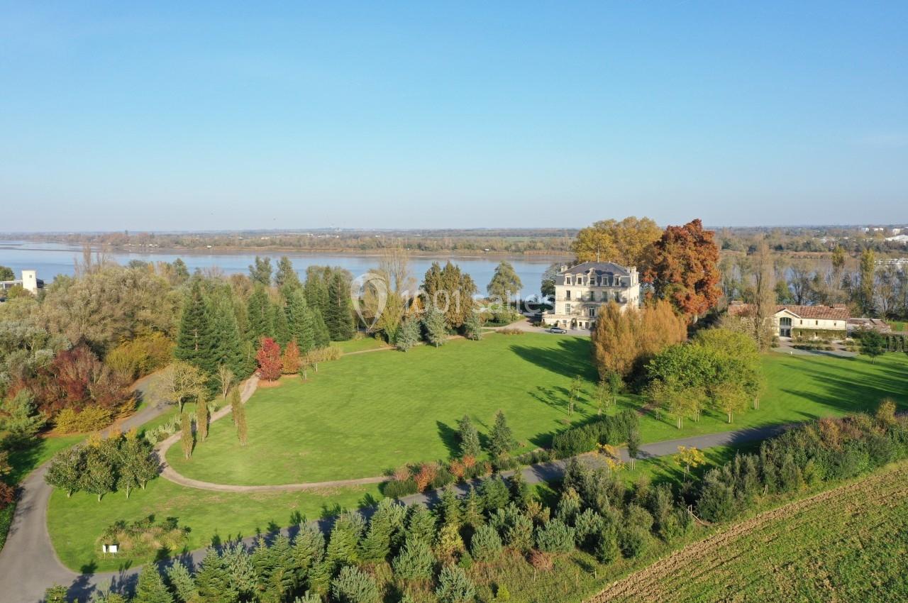 Vue aérienne d'un grand domaine avec pelouse, arbres, bâtiment historique et rivière en arrière-plan.