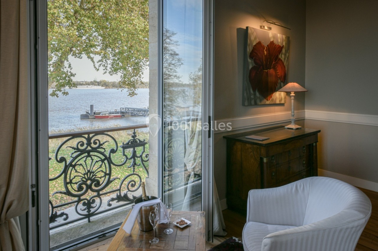 Vue depuis un salon élégant avec fauteuil, table basse et balcon donnant sur une rivière bordée d'arbres.