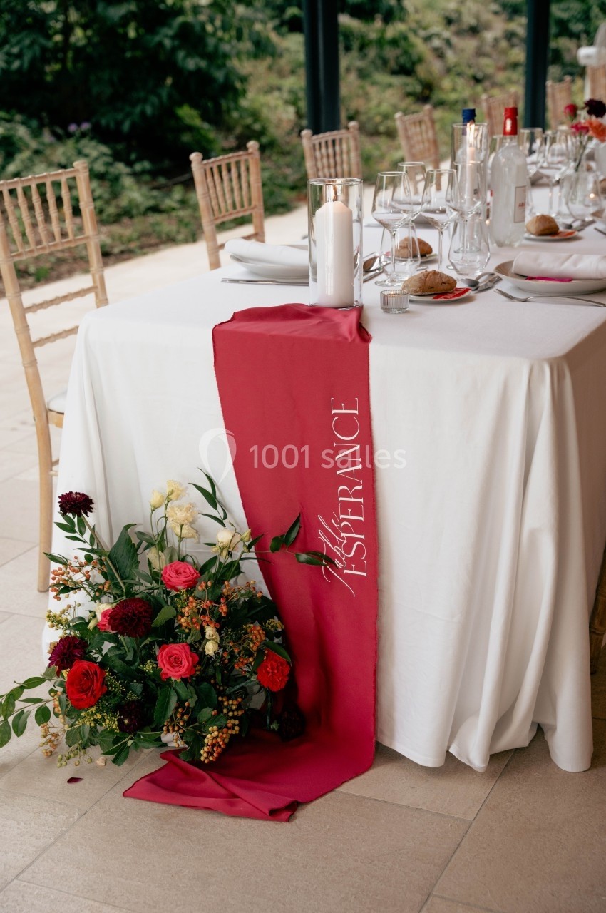 Table décorée avec une nappe blanche, un chemin de table rouge, des fleurs colorées et des couverts élégants.