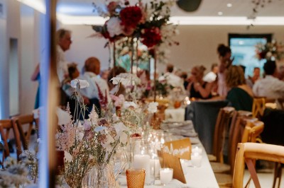 Salle de réception décorée avec des tables rondes, nappes blanches, chandeliers et arrangements floraux élégants.