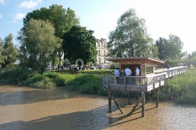 Vue d'une salle de bain avec double vasque en bois et d'une chambre lumineuse avec parquet et grandes fenêtres.