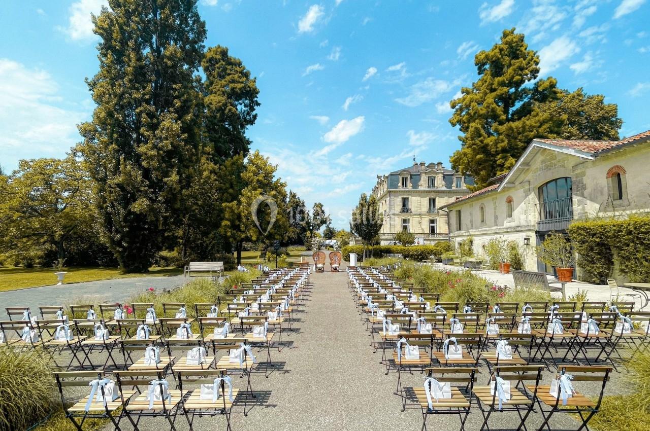 Chaises alignées en extérieur pour une cérémonie, avec un bâtiment ancien et des arbres en arrière-plan.
