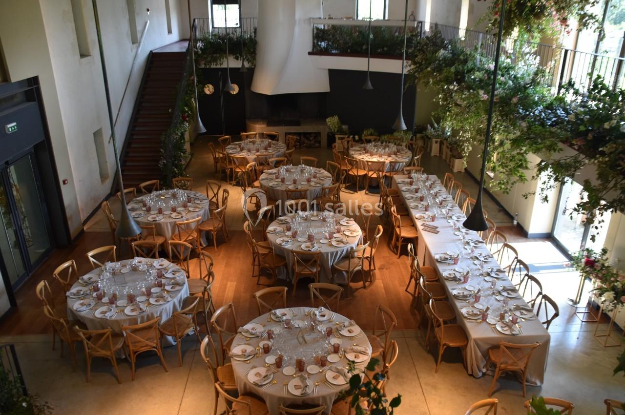 Salle de réception lumineuse avec tables rondes et rectangulaires dressées, entourées de chaises en bois.