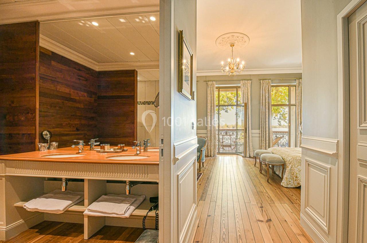 Vue d'une salle de bain avec double vasque en bois et d'une chambre lumineuse avec parquet et grandes fenêtres.