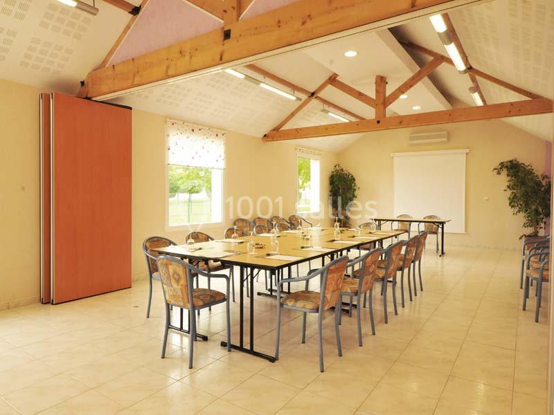 Salle de réunion lumineuse avec tables disposées en U, chaises, écran de projection et grandes fenêtres donnant sur l…