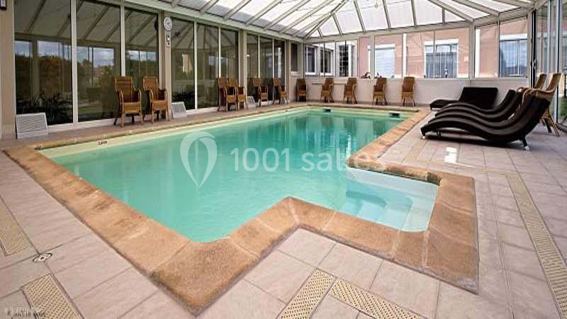 Piscine intérieure avec chaises longues en bois et baies vitrées laissant entrer la lumière naturelle.