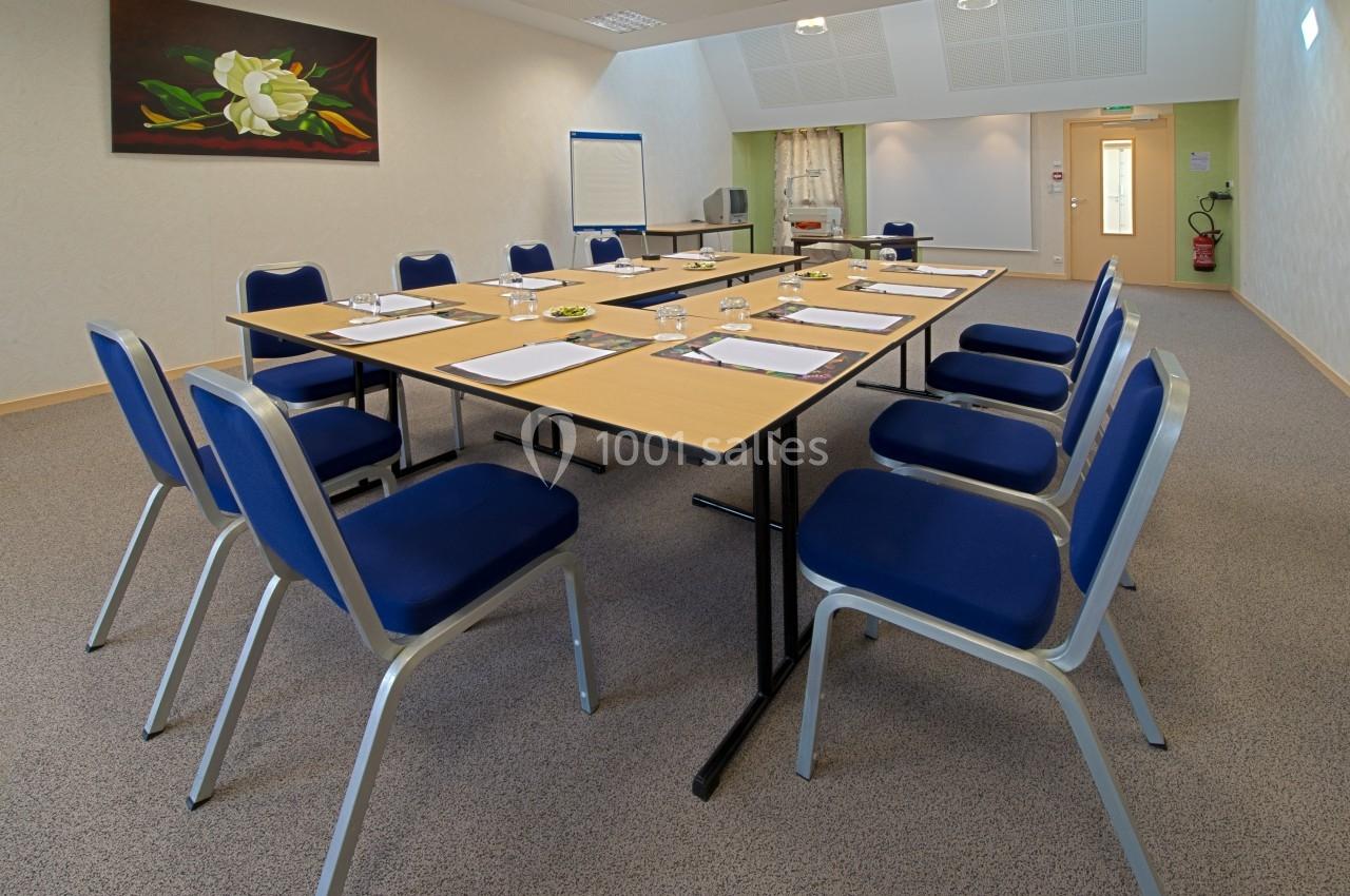 Salle de réunion avec une grande table rectangulaire, des chaises bleues, un tableau de conférence et un tableau mural.