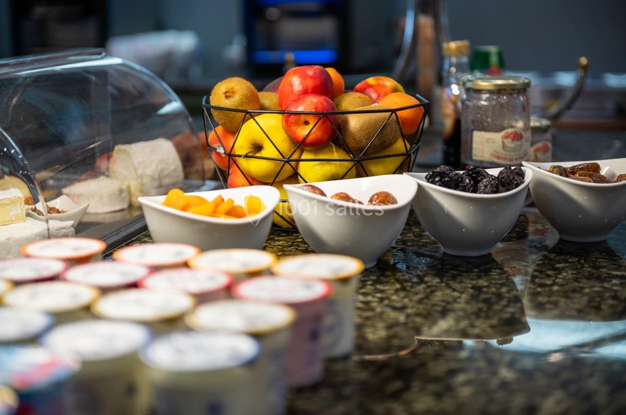 Panier de fruits frais et bols de fruits secs disposés sur un comptoir avec des yaourts et des confitures.
