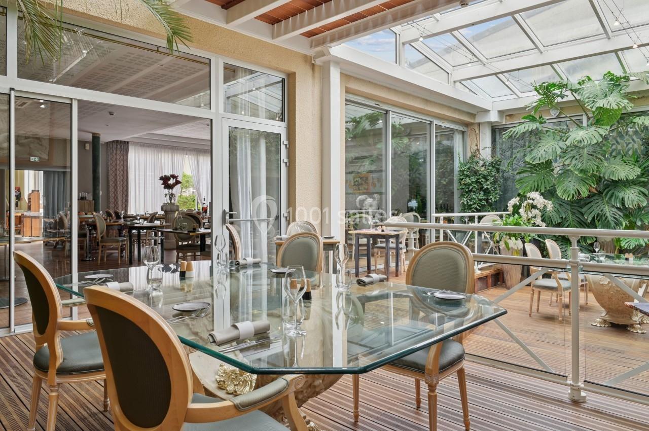 Salle à manger lumineuse avec une table en verre, chaises élégantes et vue sur une terrasse entourée de plantes.