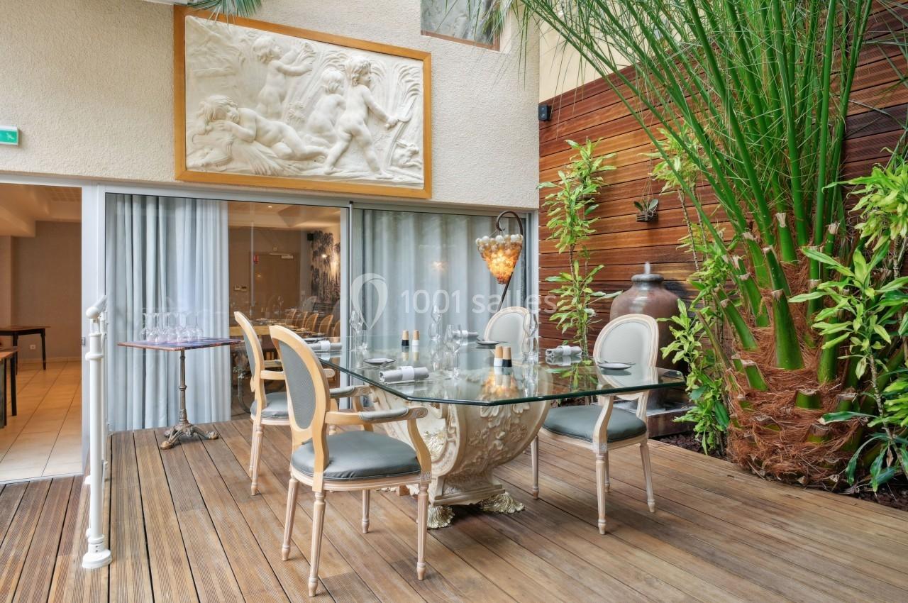 Salle à manger élégante avec table en verre, chaises classiques, plantes luxuriantes et sculpture murale en arrière-plan.