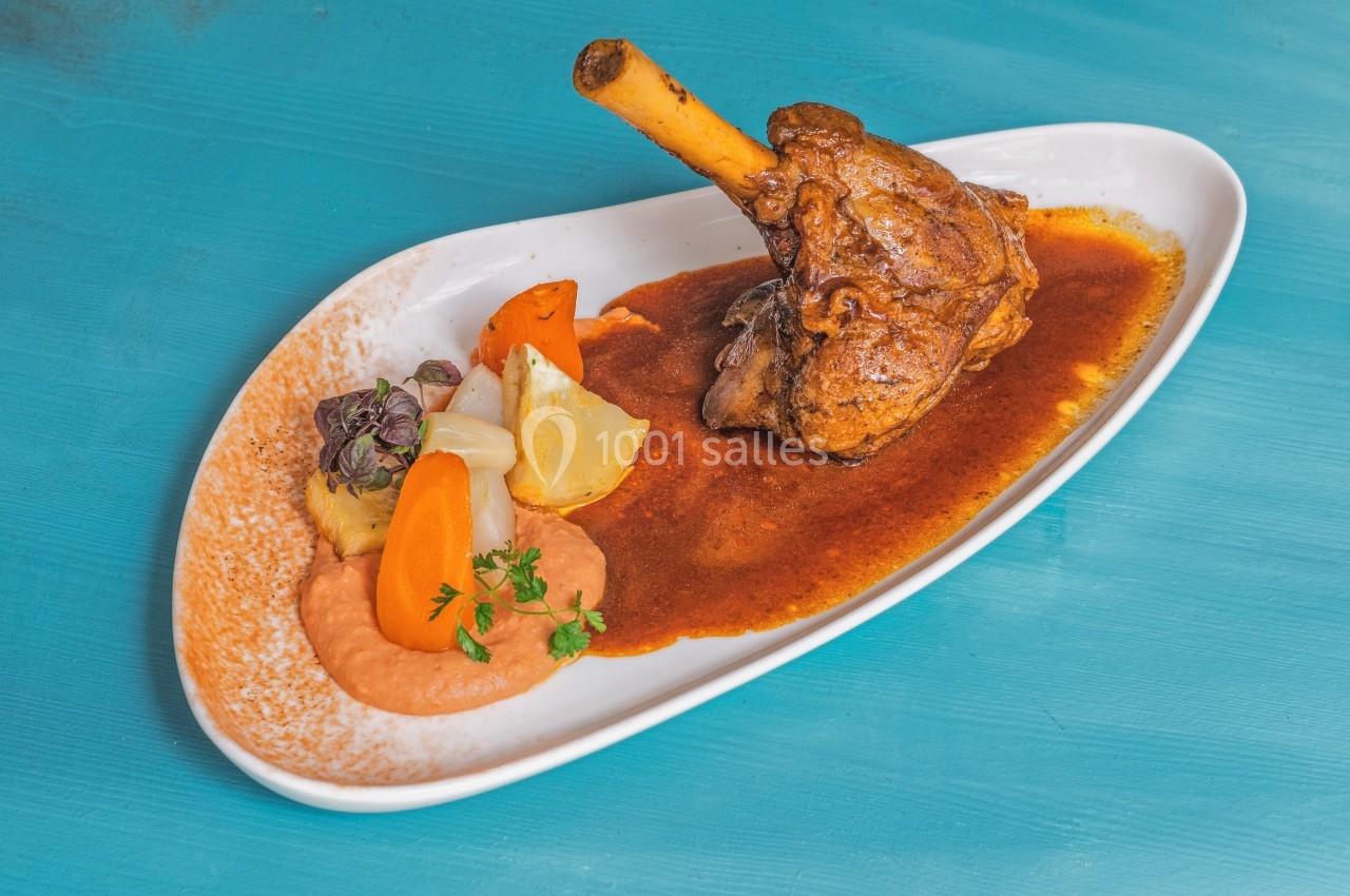 Plat de jarret d'agneau braisé servi avec purée, légumes colorés et sauce, présenté sur une assiette blanche.