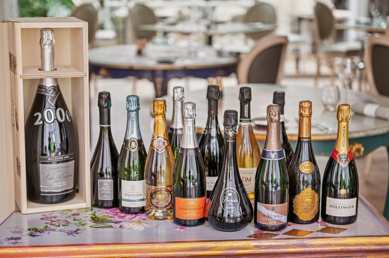 Bouteilles de champagne variées alignées sur une table décorée, avec une caisse en bois contenant une bouteille millésimée.