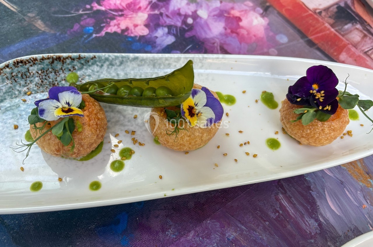 Assiette de présentation avec trois bouchées garnies de fleurs comestibles, pois verts et sauce verte.